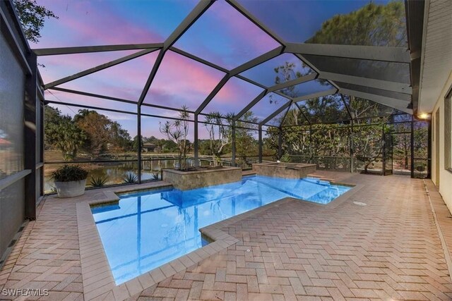 pool at dusk with a patio, a water view, glass enclosure, and an in ground hot tub