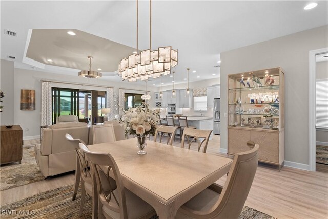 dining area featuring a raised ceiling, a wealth of natural light, light hardwood / wood-style floors, and french doors