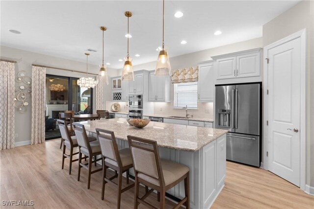 kitchen with a kitchen island, light stone countertops, appliances with stainless steel finishes, and hanging light fixtures