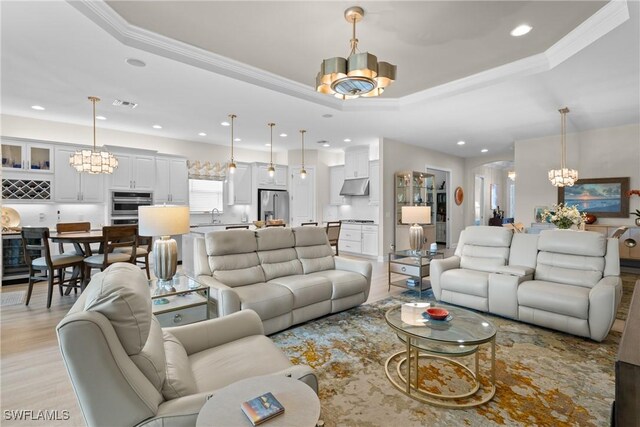 living room featuring a raised ceiling, crown molding, light wood-type flooring, and a chandelier