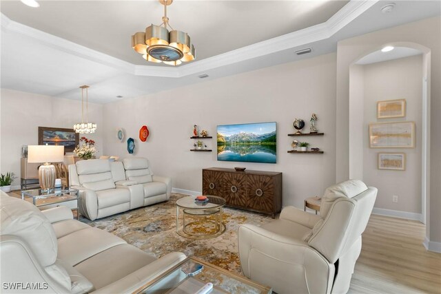 living room featuring ornamental molding, a tray ceiling, light hardwood / wood-style flooring, and a notable chandelier