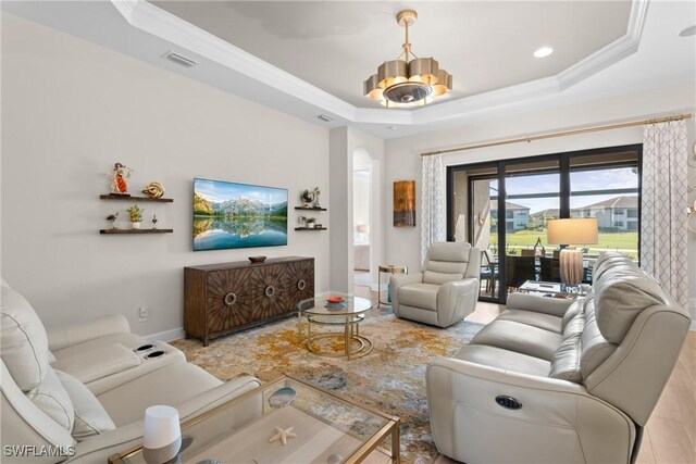 living room with a tray ceiling, ornamental molding, and a chandelier