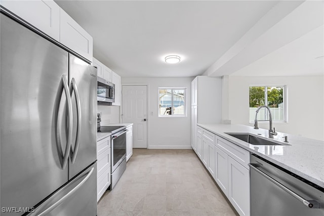 kitchen featuring stainless steel appliances, white cabinets, a sink, and light stone counters