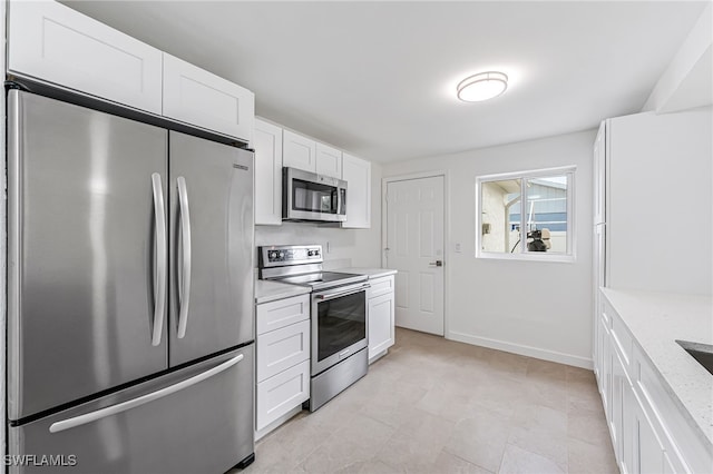 kitchen with baseboards, appliances with stainless steel finishes, light stone countertops, and white cabinets