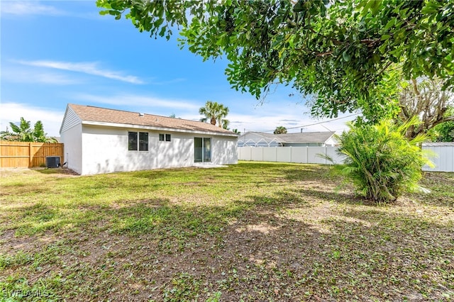 back of house featuring central AC, a yard, a fenced backyard, and stucco siding