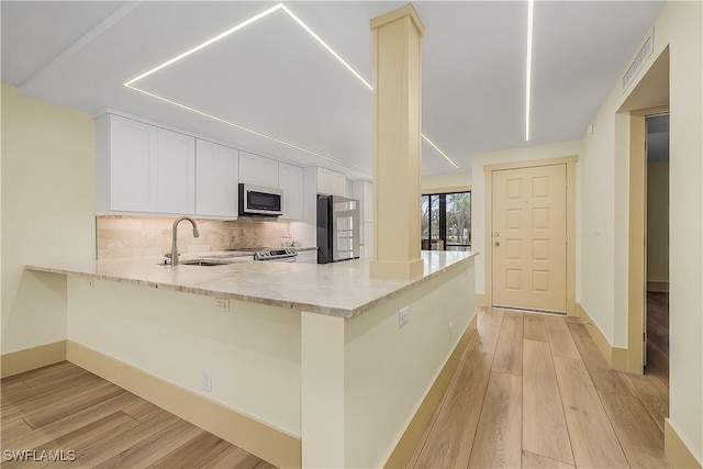 kitchen with kitchen peninsula, appliances with stainless steel finishes, sink, light wood-type flooring, and light stone counters