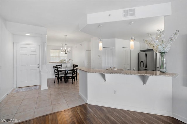 kitchen featuring stainless steel fridge with ice dispenser, white cabinets, kitchen peninsula, pendant lighting, and a breakfast bar area