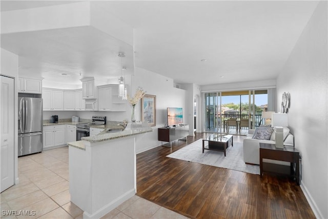 kitchen with kitchen peninsula, white cabinetry, light stone countertops, and appliances with stainless steel finishes