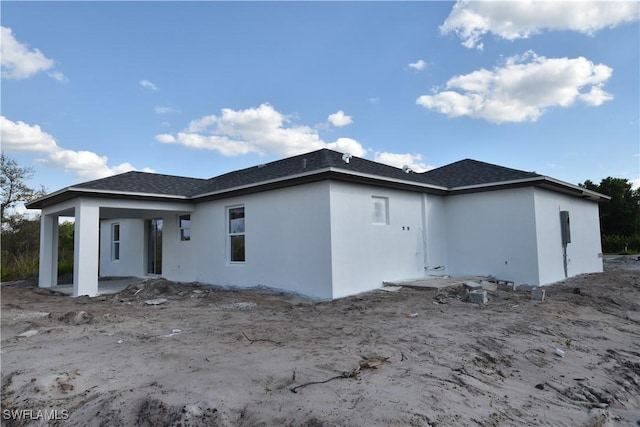 rear view of property featuring a shingled roof, a patio area, and stucco siding