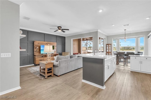 kitchen with pendant lighting, white cabinets, a kitchen island with sink, ceiling fan, and light hardwood / wood-style flooring