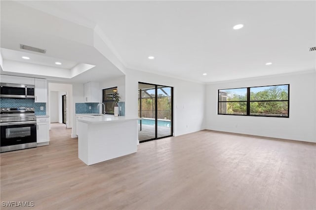 kitchen featuring stainless steel appliances, white cabinets, open floor plan, light countertops, and tasteful backsplash