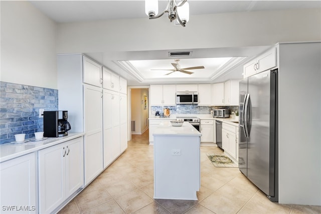 kitchen with a center island, appliances with stainless steel finishes, a tray ceiling, white cabinets, and backsplash