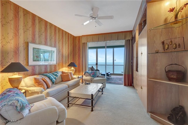 carpeted living room with ceiling fan and a water view