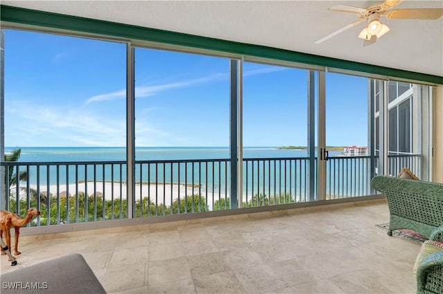 unfurnished sunroom featuring a water view, a view of the beach, and ceiling fan