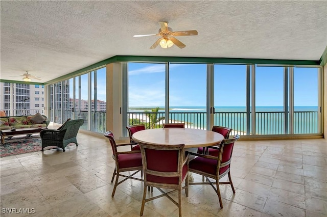 dining space with a textured ceiling, a healthy amount of sunlight, a water view, and floor to ceiling windows