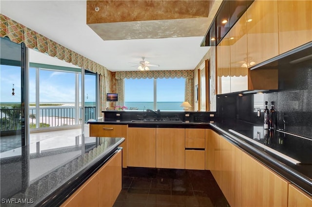 kitchen featuring dark tile patterned floors, black electric stovetop, sink, dark stone countertops, and ceiling fan