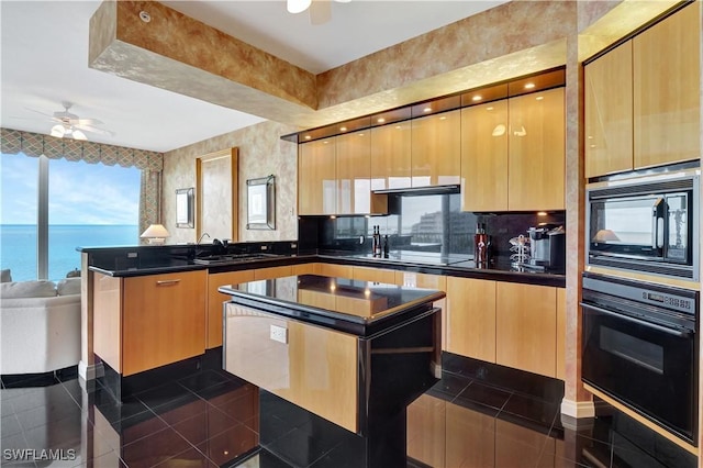 kitchen with ceiling fan, black appliances, a center island, and a water view