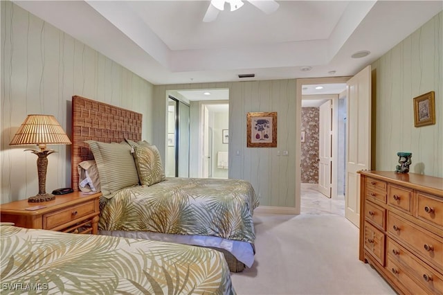 carpeted bedroom featuring ceiling fan, a raised ceiling, and ensuite bath