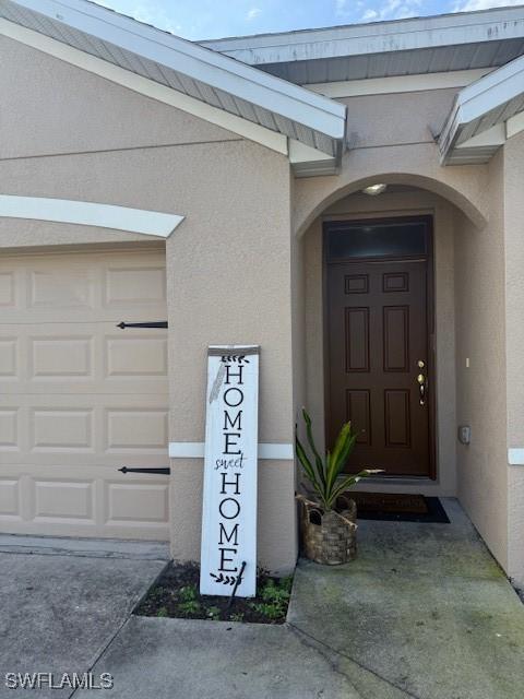 doorway to property with a garage, concrete driveway, and stucco siding