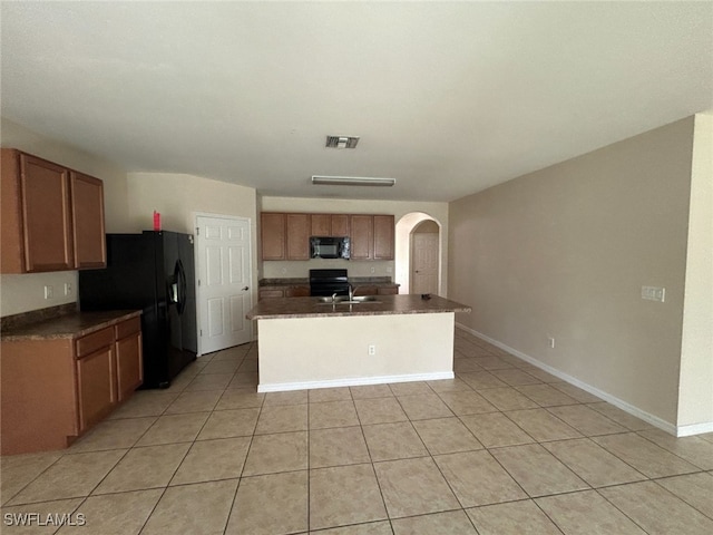 kitchen featuring arched walkways, black appliances, brown cabinetry, and dark countertops