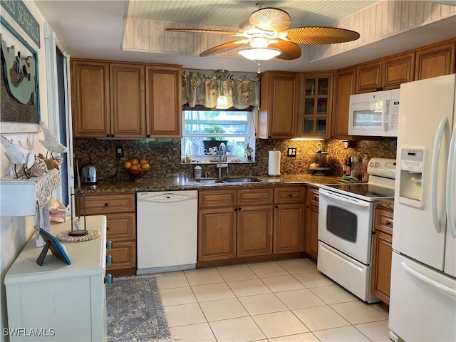 kitchen with sink, light tile patterned floors, white appliances, dark stone counters, and backsplash