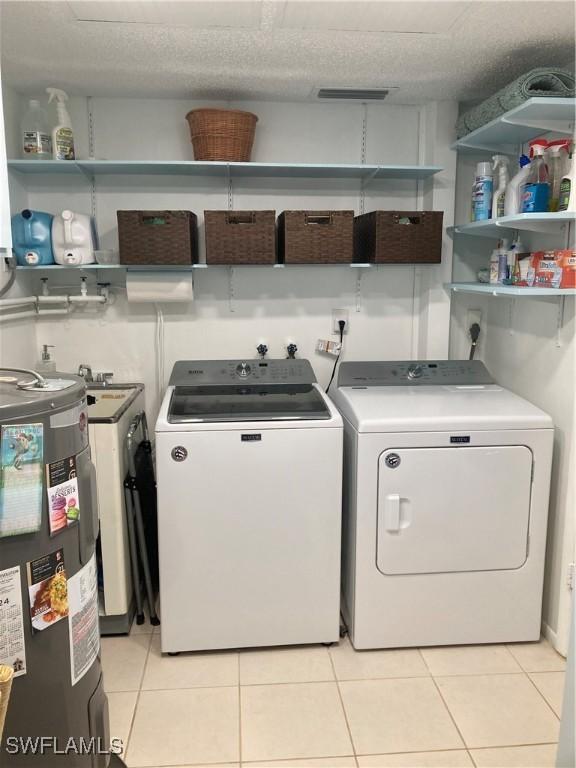 laundry room featuring electric water heater, washer and dryer, a textured ceiling, and light tile patterned flooring