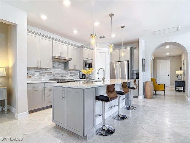 kitchen with decorative light fixtures, gray cabinets, stainless steel appliances, and an island with sink