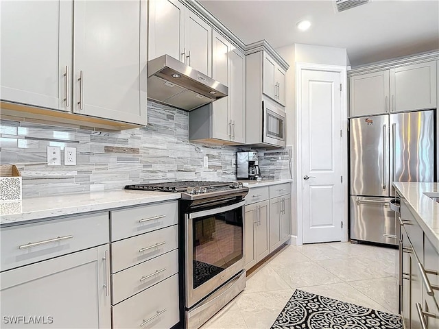 kitchen featuring stainless steel appliances, light stone countertops, gray cabinetry, and backsplash