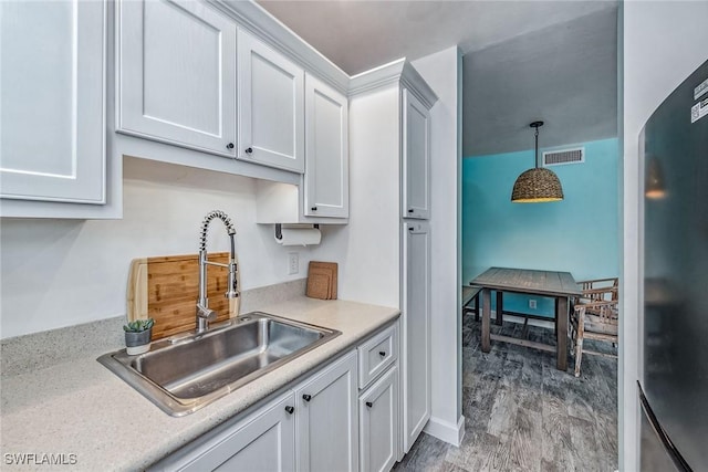 kitchen featuring pendant lighting, white cabinets, sink, light wood-type flooring, and fridge