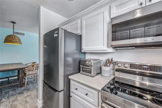 kitchen featuring light wood-type flooring, stainless steel appliances, white cabinetry, and pendant lighting