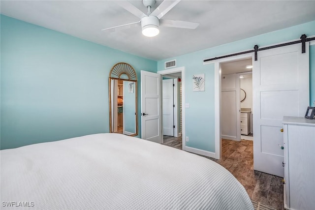 bedroom with ceiling fan, a barn door, dark wood-type flooring, and ensuite bath