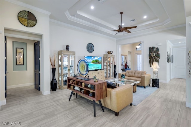 living room with light hardwood / wood-style flooring, ceiling fan, a high ceiling, a tray ceiling, and ornamental molding