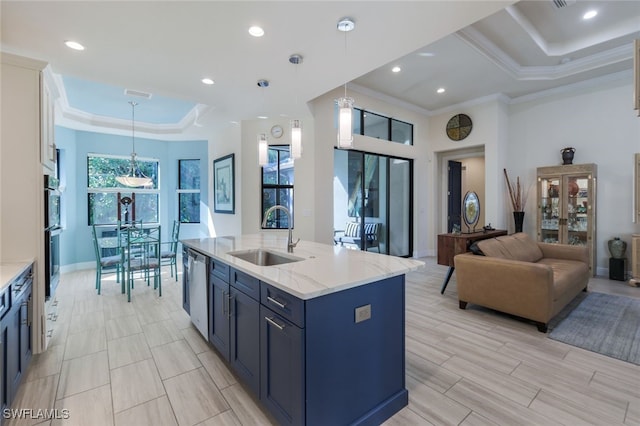 kitchen featuring sink, a center island with sink, a tray ceiling, pendant lighting, and light stone countertops