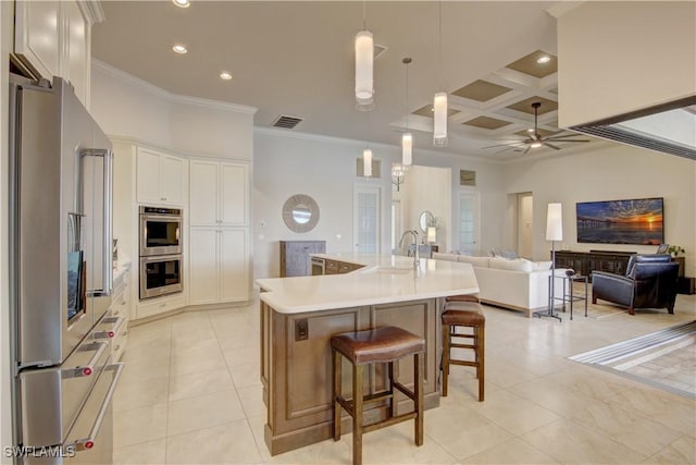 kitchen with sink, appliances with stainless steel finishes, white cabinetry, coffered ceiling, and an island with sink