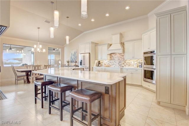 kitchen with lofted ceiling, decorative light fixtures, a large island with sink, custom range hood, and stainless steel appliances