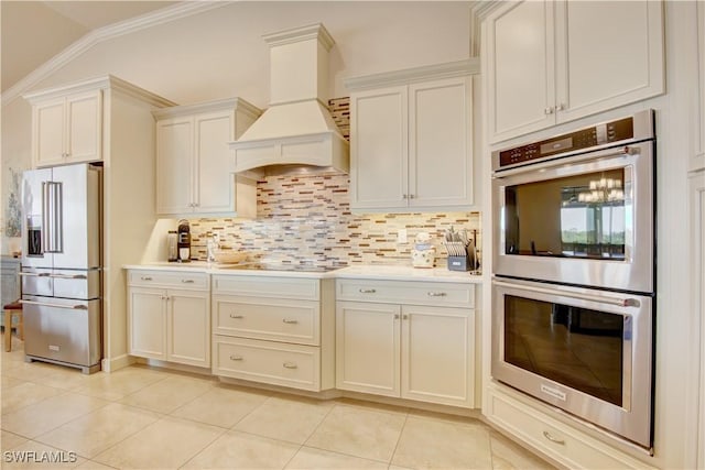 kitchen featuring light tile patterned floors, appliances with stainless steel finishes, white cabinets, decorative backsplash, and custom exhaust hood