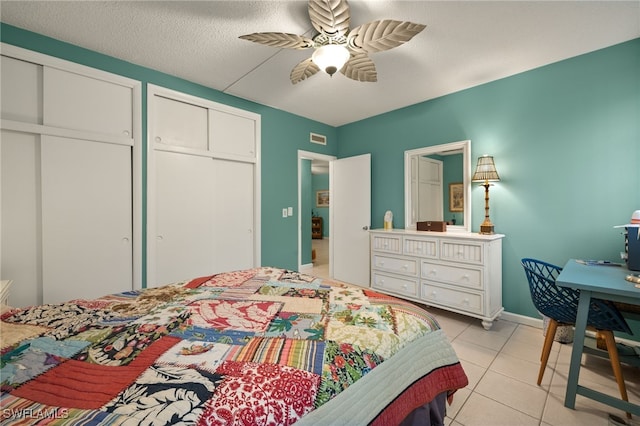 bedroom featuring multiple closets, light tile patterned floors, a textured ceiling, and ceiling fan