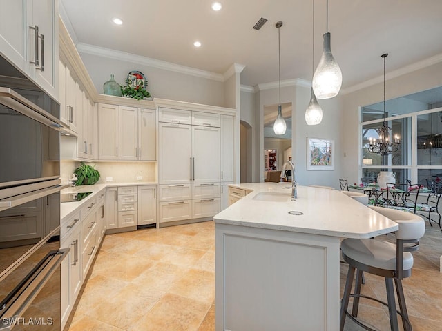 kitchen with decorative light fixtures, an island with sink, sink, light stone countertops, and black electric cooktop