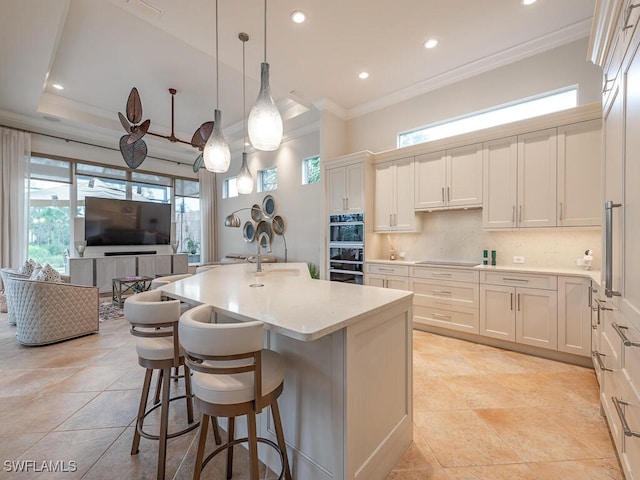 kitchen with pendant lighting, crown molding, backsplash, black appliances, and a center island with sink