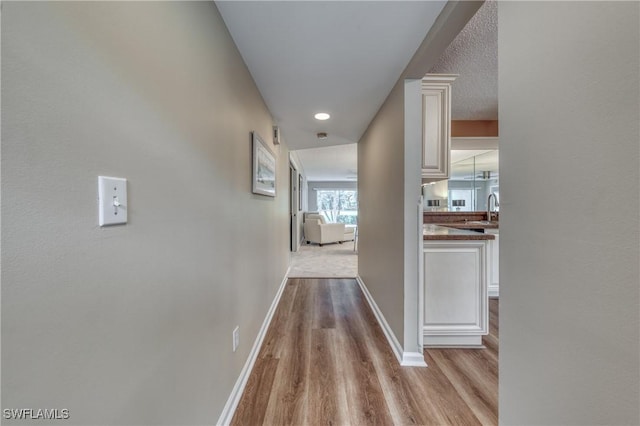 hallway featuring light wood finished floors, a sink, and baseboards