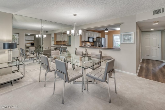 dining space with a textured ceiling, a notable chandelier, visible vents, baseboards, and carpet