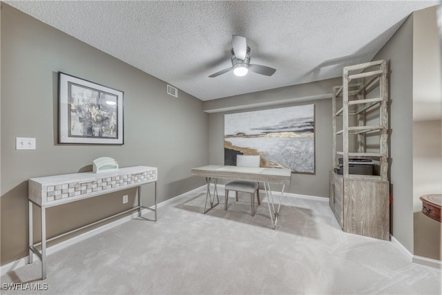 carpeted office space with a textured ceiling, baseboards, visible vents, and a ceiling fan