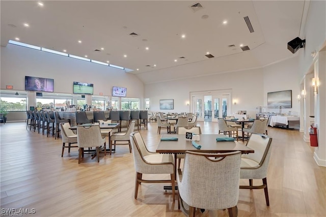 dining room with light wood-style floors, a high ceiling, and visible vents