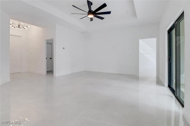 empty room featuring a tray ceiling and ceiling fan with notable chandelier