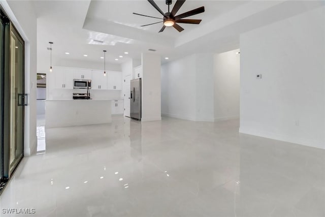 unfurnished living room featuring a raised ceiling and ceiling fan