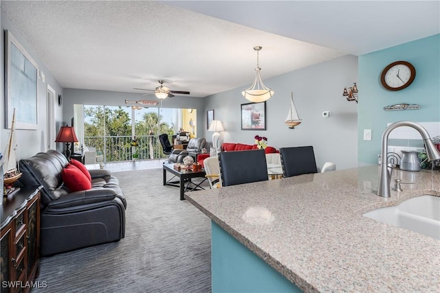 kitchen featuring ceiling fan, sink, decorative light fixtures, dark colored carpet, and a textured ceiling