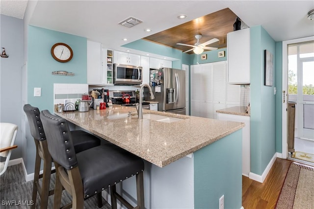 kitchen with kitchen peninsula, light stone counters, white cabinets, and appliances with stainless steel finishes