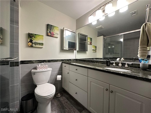 bathroom with hardwood / wood-style floors, tile walls, vanity, toilet, and a shower with door