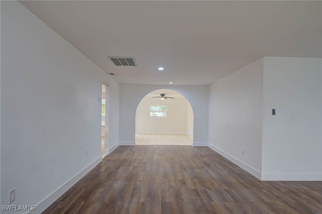 unfurnished room with dark wood-style floors, arched walkways, visible vents, and baseboards