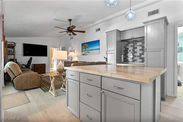 kitchen with lofted ceiling, butcher block counters, gray cabinetry, a kitchen island, and light hardwood / wood-style floors